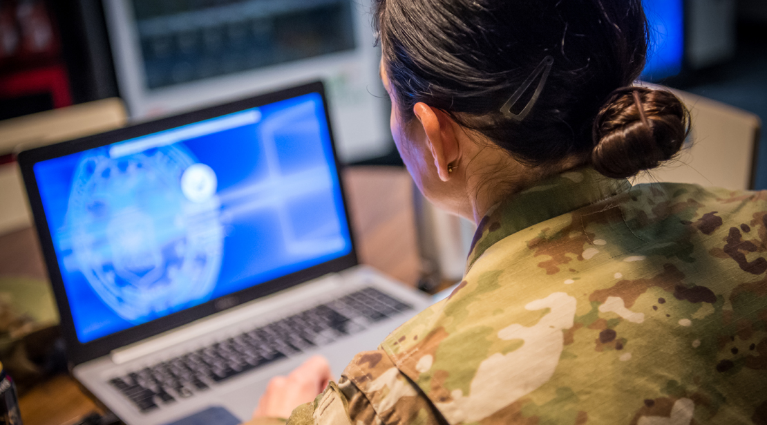 Female student in military fatigues working at a laptop on an online class. 