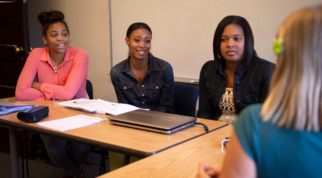 Four female students in a classroom having a discussion. 