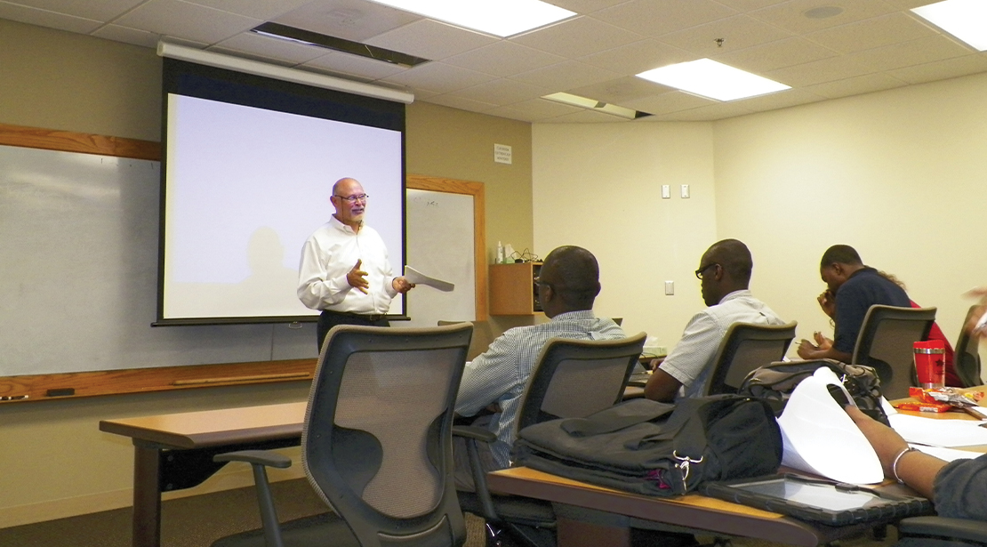 Male students in front of a classroom lecturing to several students. 