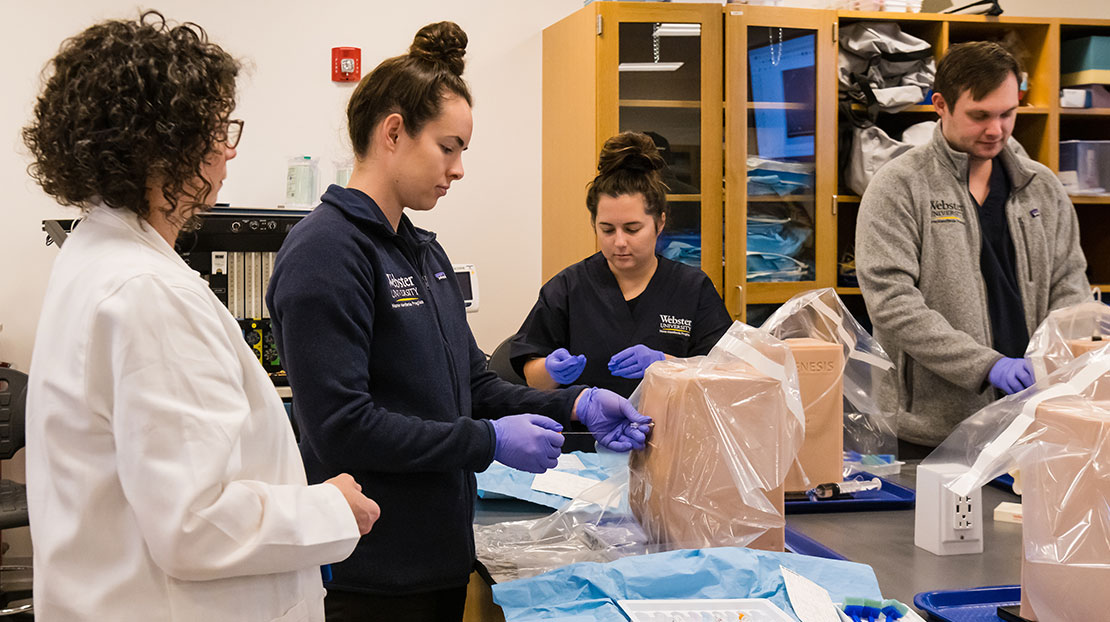 Professor instructs three Webster DNAP students through hands-on simulated spinal punctures