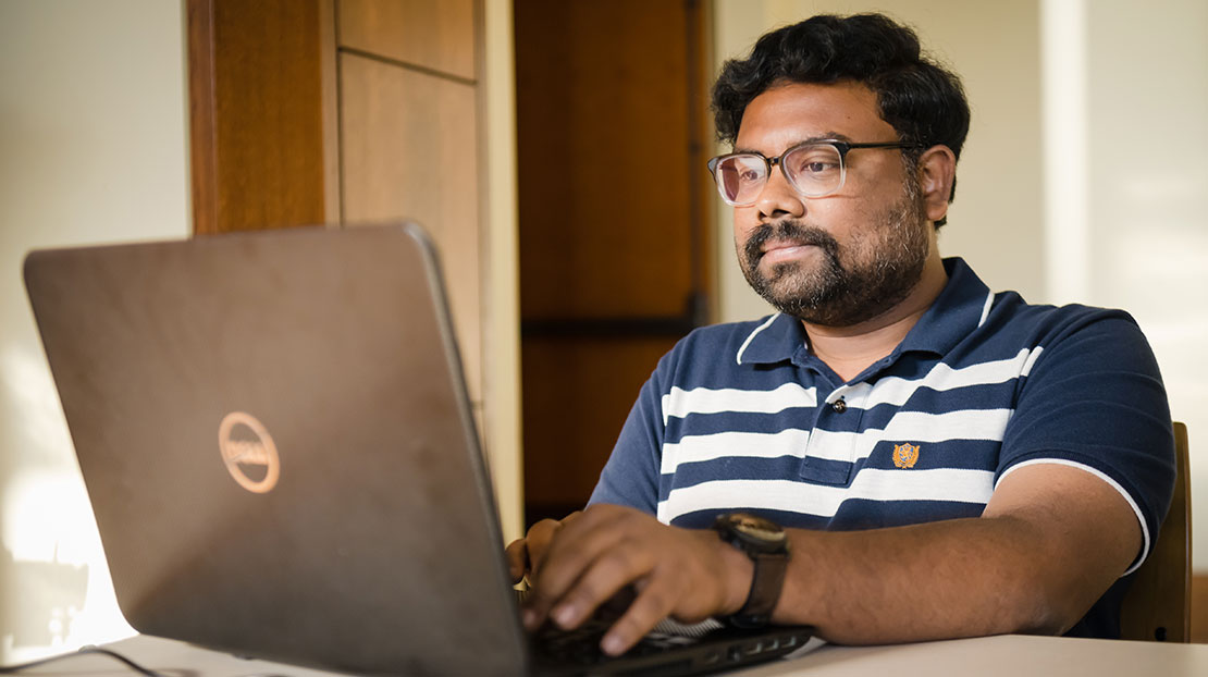 Male student with dark complexion works on laptop at table