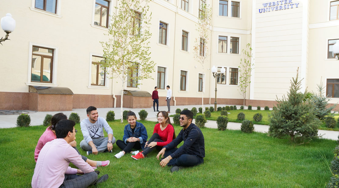 A group of students sits in a semi-circle in the grass at our Tashkent campus. 