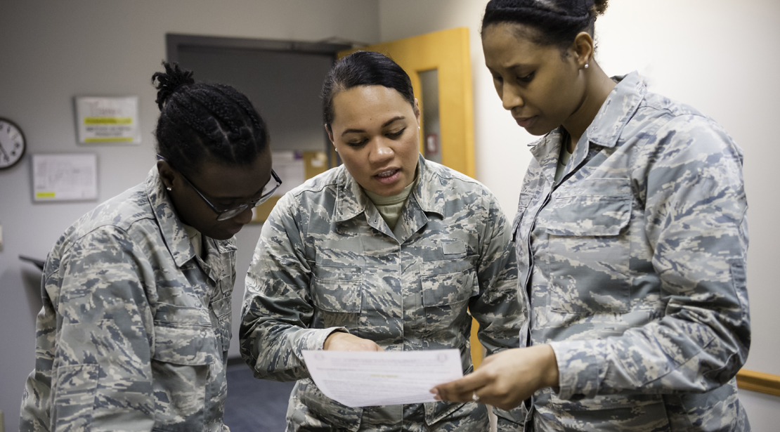 Three female students in military fatigues standing together looking at and discussing a paper one of them is holding. 