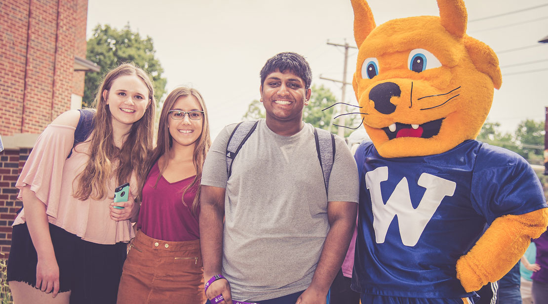 Gorlok poses outside with a diverse group of two female and one male student.