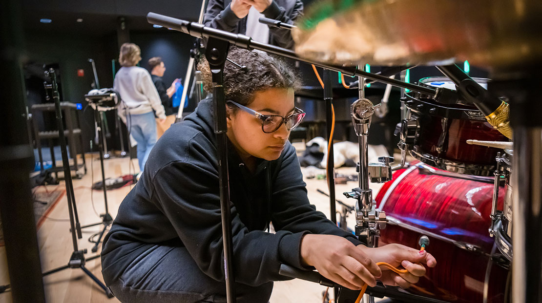 student attaching sound wiring to drum for live music recording