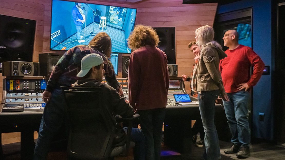 students around AXS sound board looking at sound booth on monitor