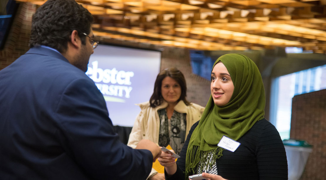student in hijab shaking hands with a man in a suit