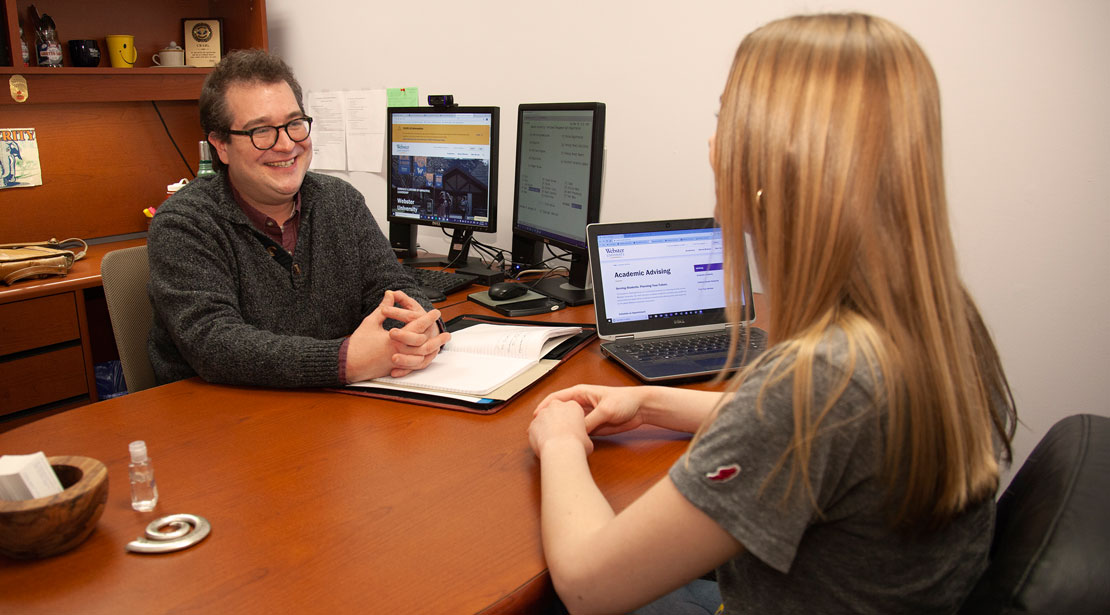 Academic advisor and student in conversation at a desk.