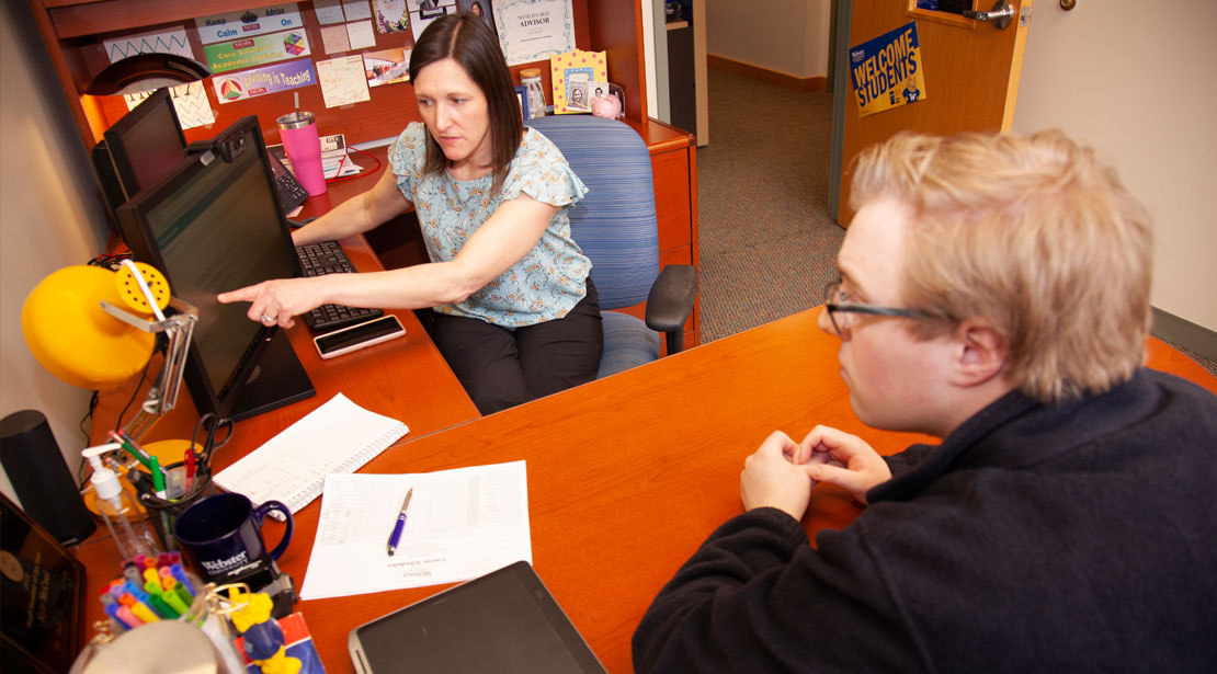 The academic advisor points to a computer screen while talking with a student during an advising session.