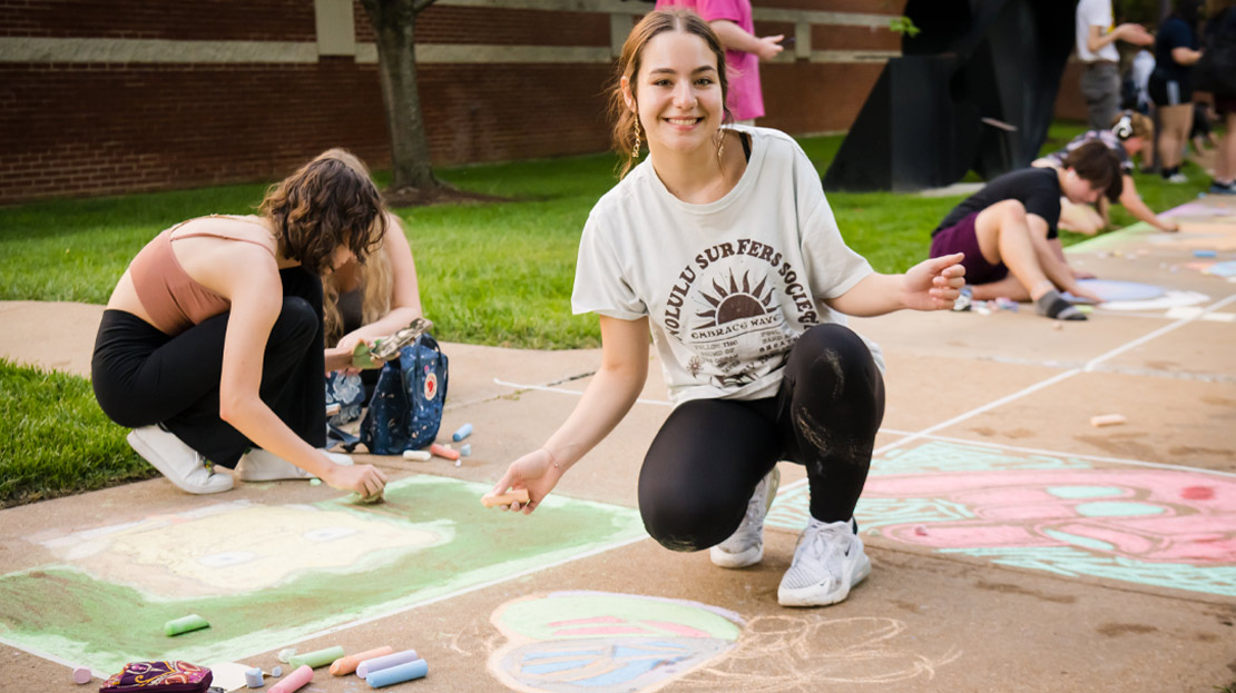 A student poses while kneeling over their chalk art.