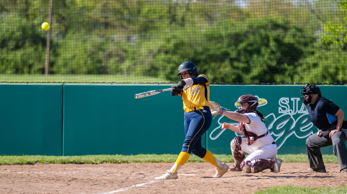 A softball player hits the ball while at bat.