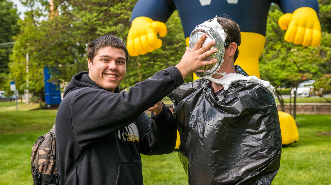 A male student pie-ing a professor in the face.