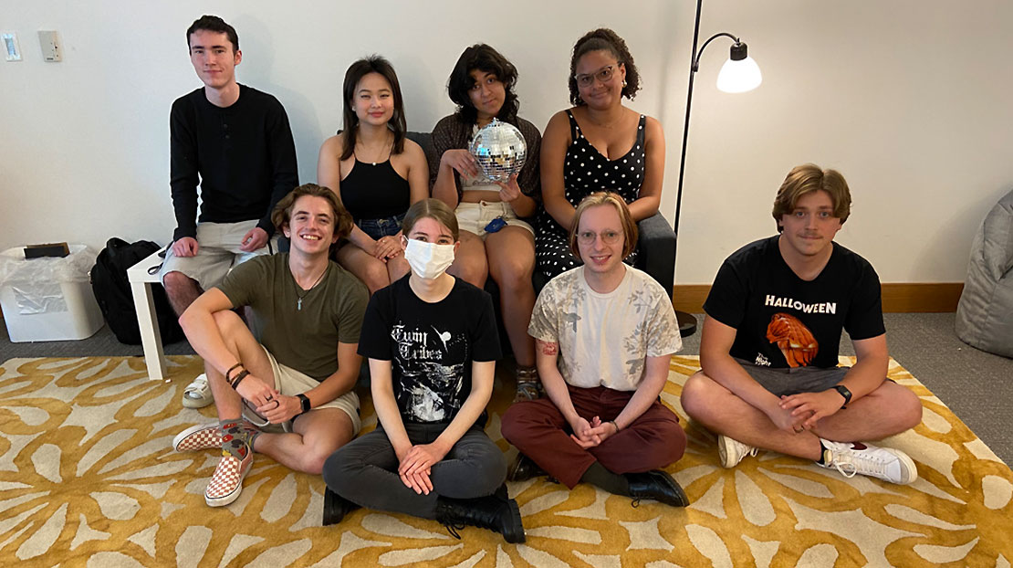 Group of students sitting on chairs and cross-legged on floor smiling