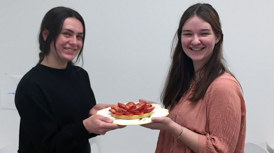 Two students hold a plate with a strawberry tart on it