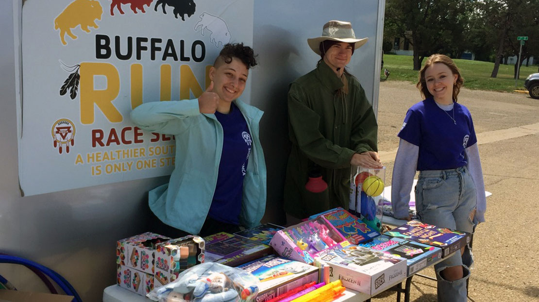 Three students stand around table with kids toys and gifts at charity event