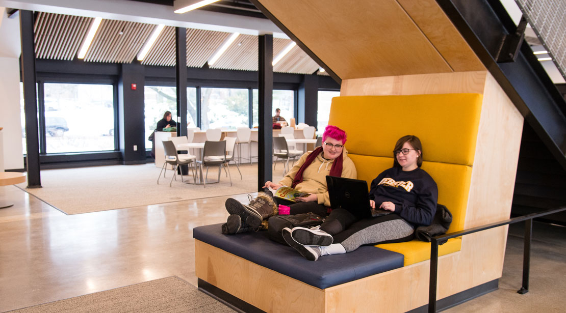 student sitting on bench below stairs in Media Commons