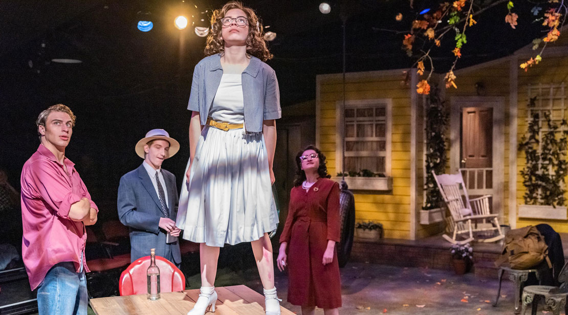 The actress stands on a picnic table looking upwards while two actors and an actress look on.