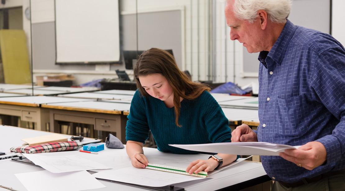 A faculty member mentors a student through her assignment in a classroom.