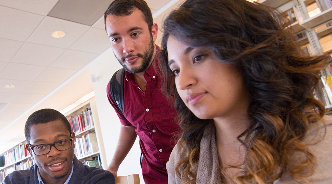 Three students work closely with each other while reviewing a file on a computer.