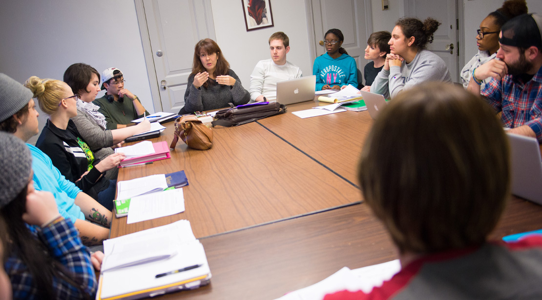 A group of students takes part in a symposium with a faculty member.