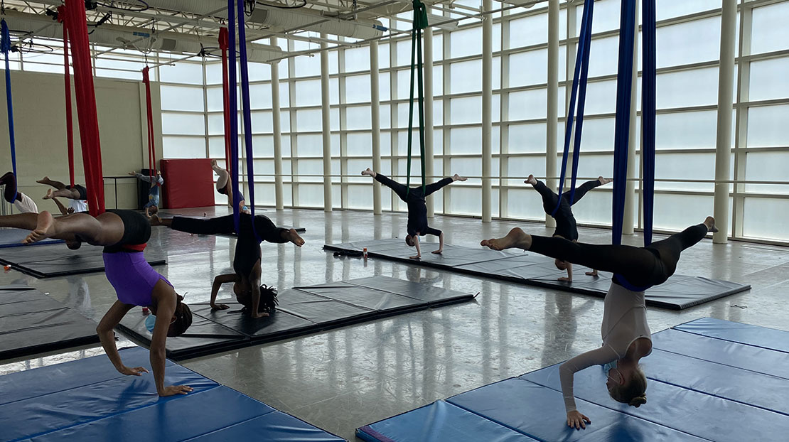 Dancers on aerial silk ribbons in inverted splits.