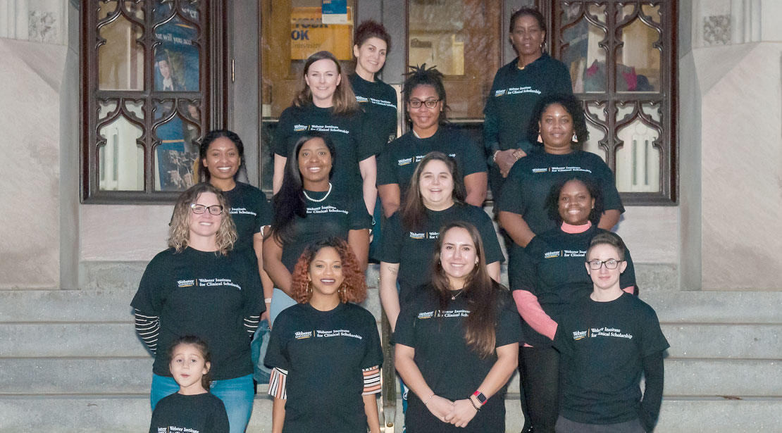 Fall 2021 scholars and Counseling professors wearing black t-shirts with the Webster Institute for Clinical Study logo stand in four rows on the steps of Webster Hall.