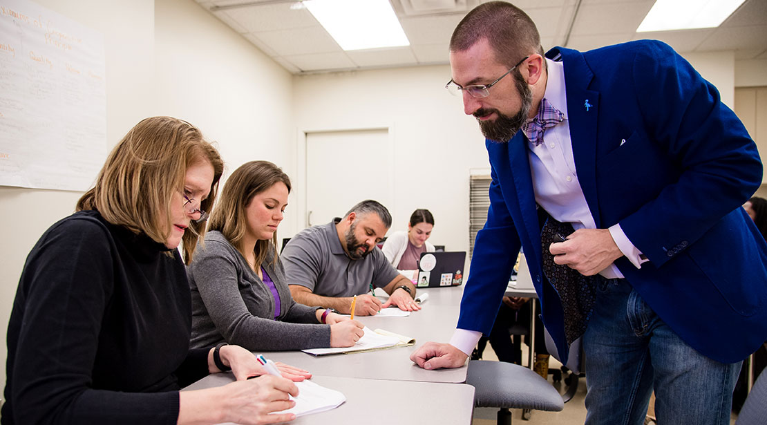 Dr. DJ Kaiser leans on long work table to look at a student's work