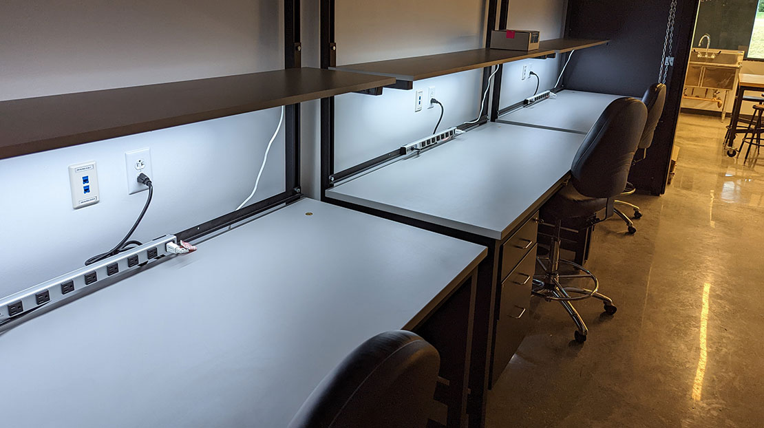 backlit workshop desks along wall with roll chairs