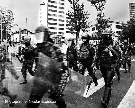 Black and white of lines of cops in riot gear walking on street, Image Credit: Nicolas Espinoza