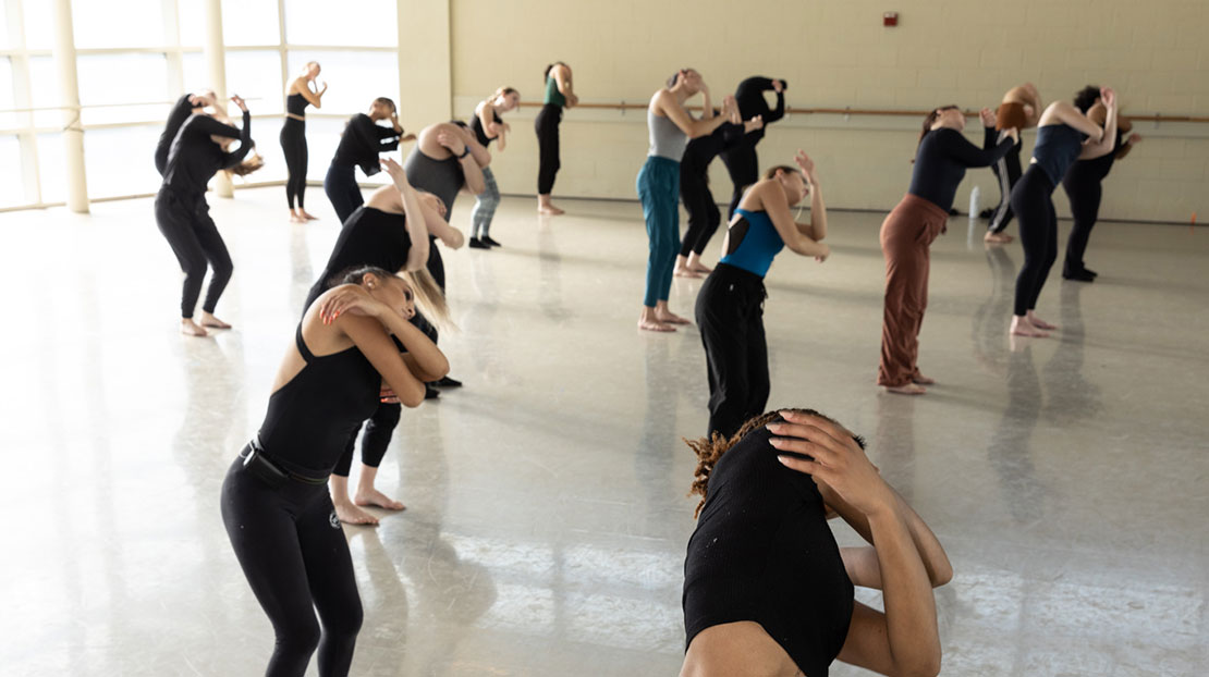 Dancers with bent knees, arms wrapped shoulder length, leaning left.