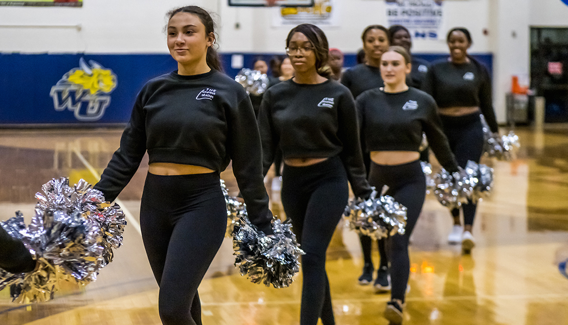 Dance team walking across the floor while holding pom poms 