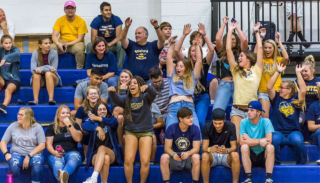Students and parents of varying ages cheering and yelling in the bleachers at a volleyball game 