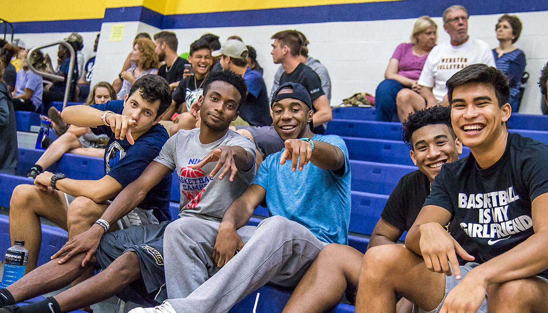 A group of young men watching volleyball game with other fans in the background 