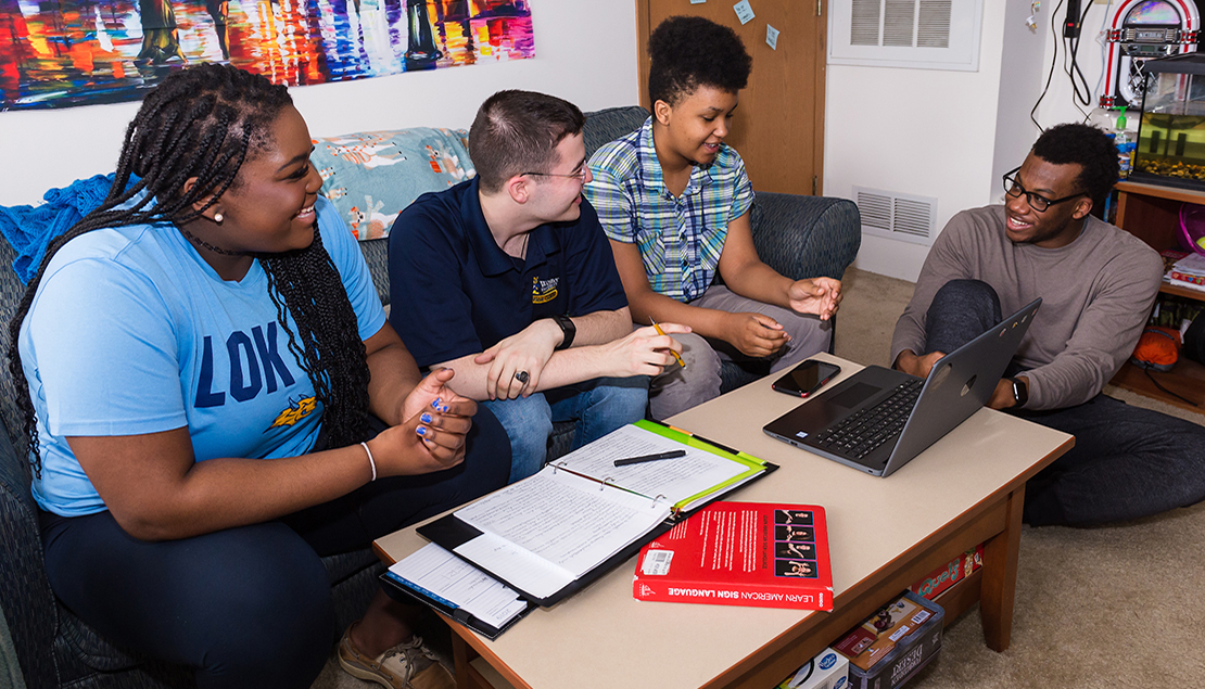 Students in dorm room talking and working on laptop