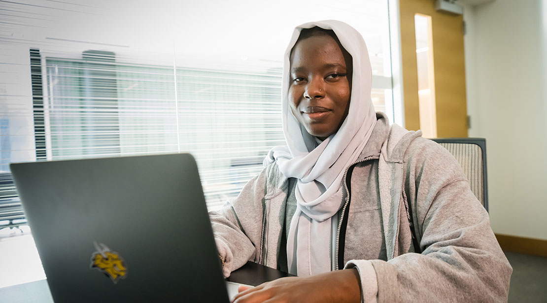 woman sitting at a laptop but smiling while facing forward