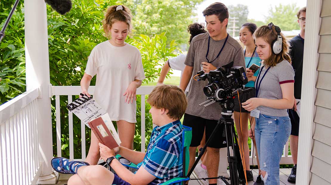 Students set up a camera for a film shot on a porch.