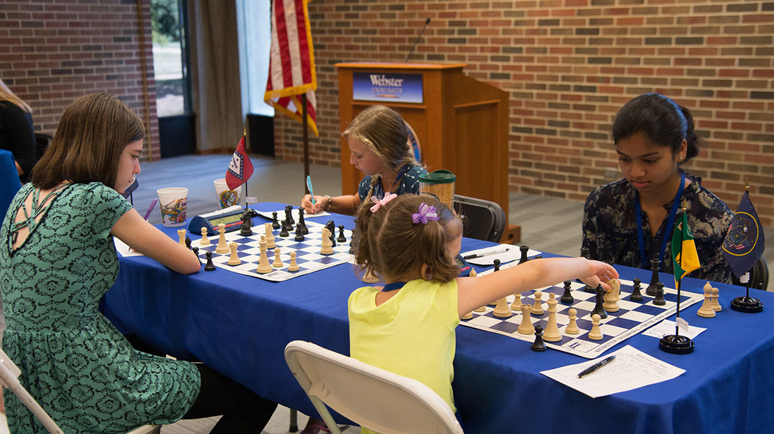 Table of four young chess players with two chess boards in play