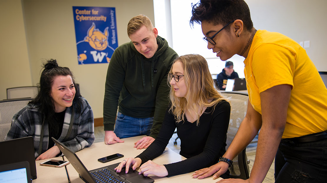 four students collaborate on two laptops