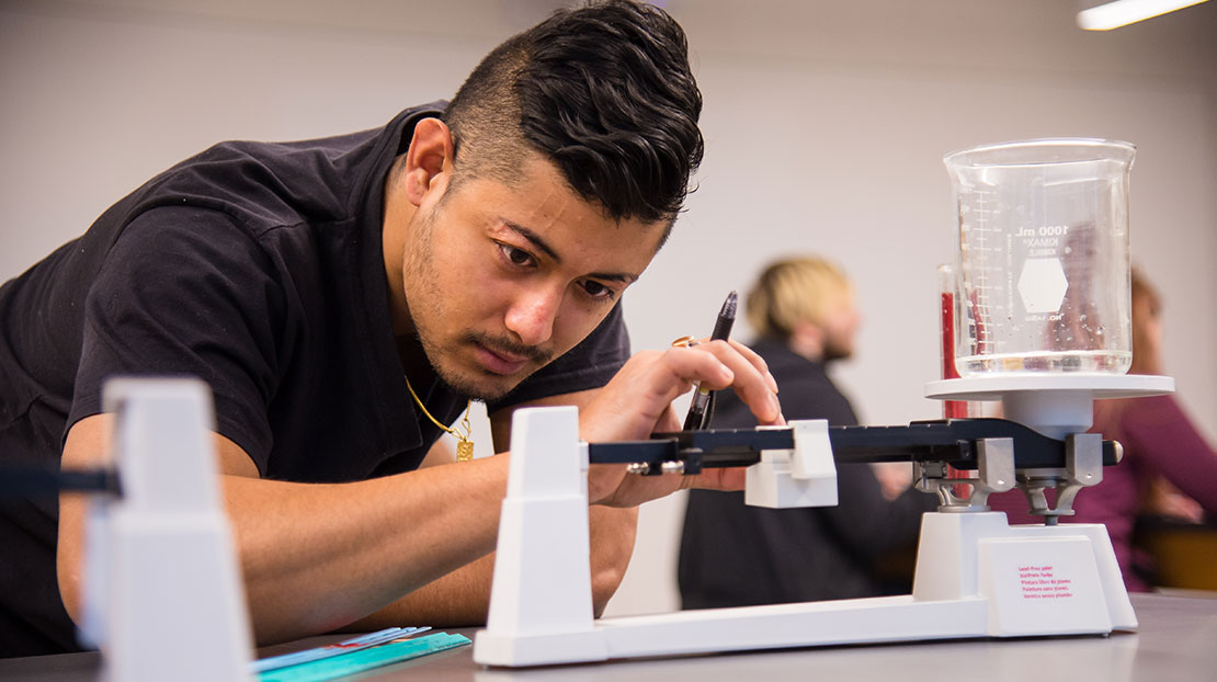 Webster student uses triple beam balance scale to weigh a glass beaker