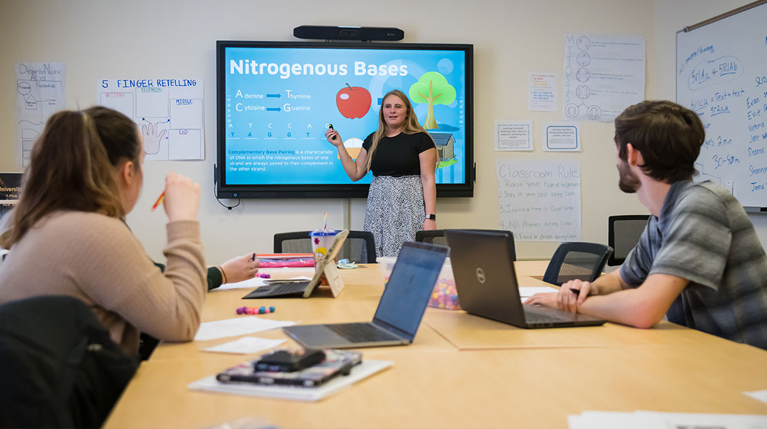 student teacher points to video slide of Nitrogenous Basis while talking to two students