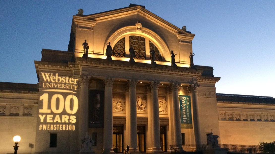 The Saint Louis Art Museum illuminated at night with "Webster University 100 Years" shining on the building.