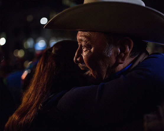 Nighttime close-up of older man with cowboy hat and woman hugging.