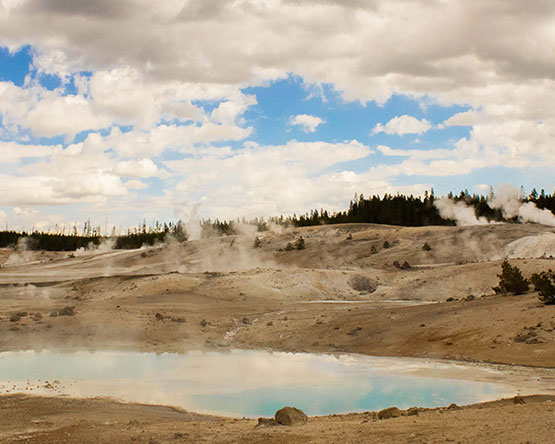 landscape of steaming hot springs and geysers, tans and blues