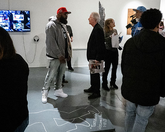 Exhibitor talks with attendee next to chalk outline art piece