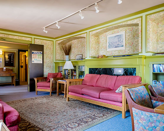 Room with pale green painted wood and floral wallpaper with red couches and chairs