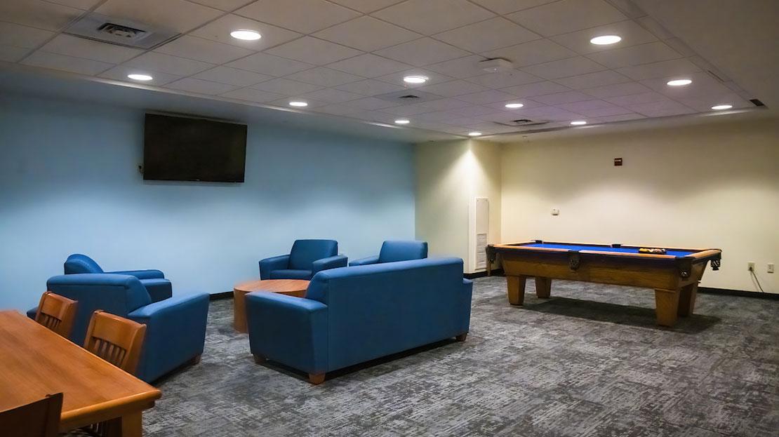 a dorm lounge with sofas, a television and pool table.