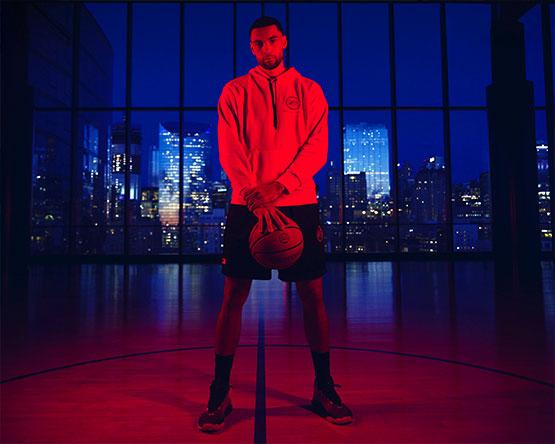 Zach LaVine stands holding basketball under red light with cityscape behind him.