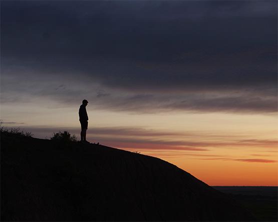 Silhouette of person standing at top of hill during sunset.