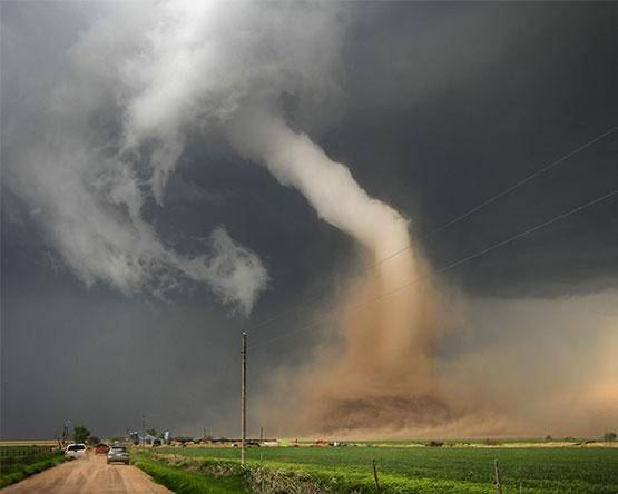A large storm cloud is coming in over a dirt road.