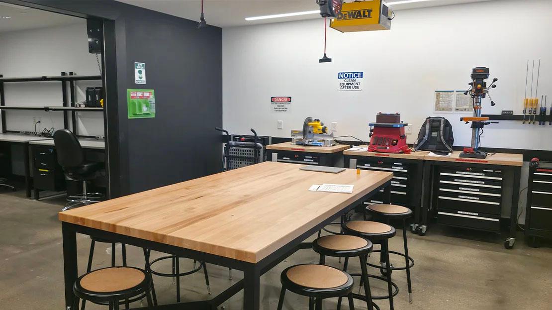 A workroom with a large flat table near a bank of cabinets with tools and machines.